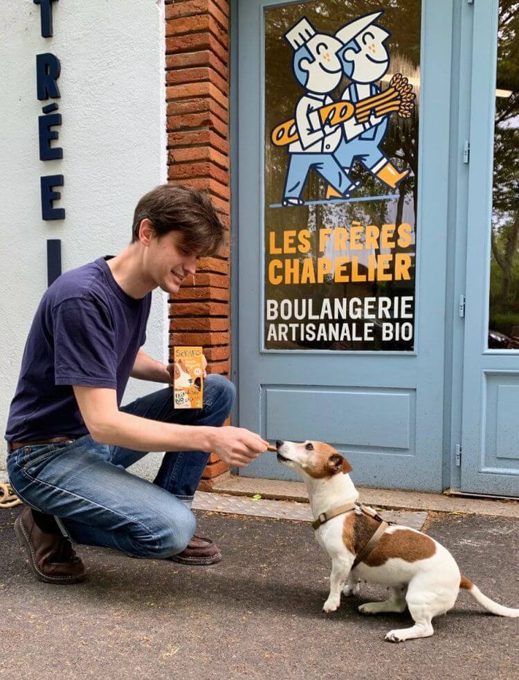 Un homme donnant un biscuit à un chien devant une boulangerie des Frères Chapelier à Toulouse